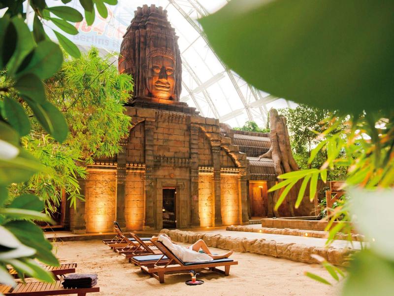 Ruhebereich mit Liegestühlen vor einer großen, beleuchteten Tempelstruktur inmitten tropischer Pflanzen.