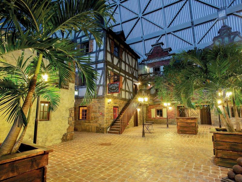 Ein beleuchteter Innenhof mit Fachwerkhäusern und grünen Palmen in Holzkästen.