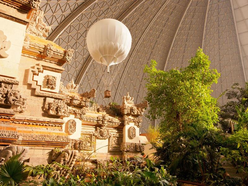 Ein tropischer Indoor-Garten mit exotischen Pflanzen und einer Heißluftballon-Dekoration unter einer großen Kuppel.