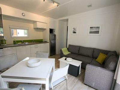 Moderner Wohn- und Essbereich mit grauem Sofa, weißem Esstisch und Küchenzeile im Hintergrund.