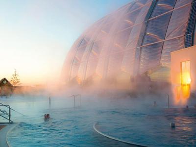 Round outdoor pool with steam at sunset next to a modern building.