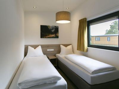 Kleines Zimmer mit zwei Einzelbetten, Nachttisch, Bild an der Wand und Fenster mit Vorhang.