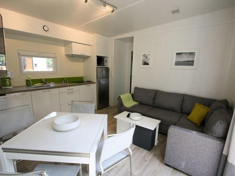 Modern living room with gray corner sofa, white dining table, and open kitchen with green countertop.