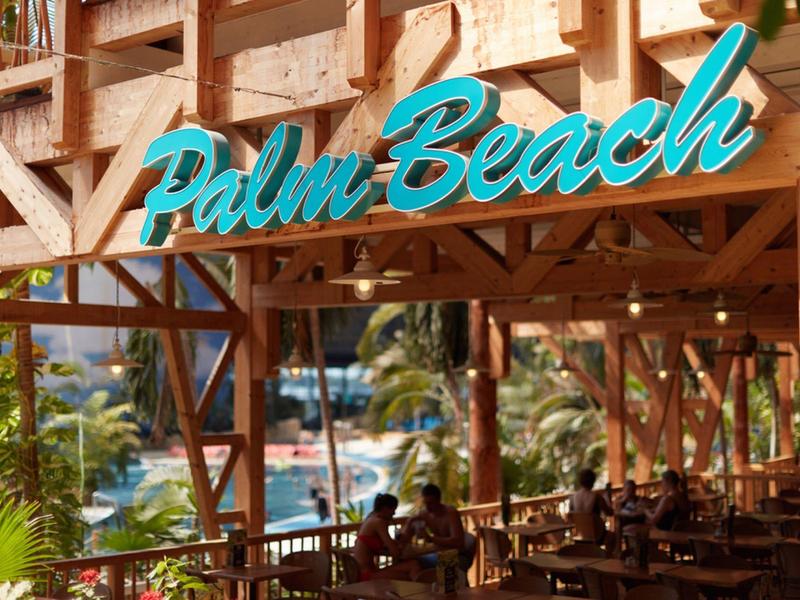 Turquoise Palm Beach sign on wooden structure outside a restaurant near a tropical setting.