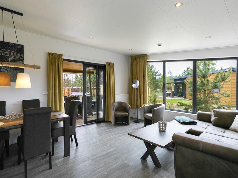 Bright living room with sofa, armchairs, dining table, and large windows overlooking garden.