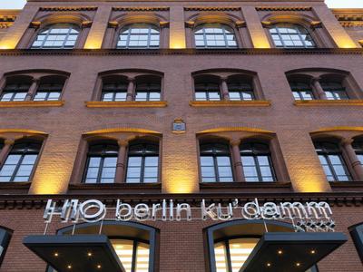 Fassade eines mehrstöckigen Backsteingebäudes mit beleuchtetem H10 Berlin Ku'damm Schild