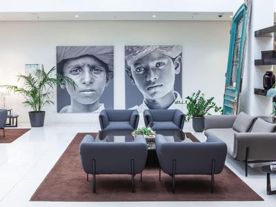 Modern eingerichteter Aufenthaltsraum mit grauen Sesseln, großem Teppich und zwei schwarz-weißen Porträtbildern.