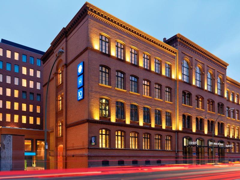 Edificio histórico de hotel iluminado al anochecer con arquitectura moderna al fondo.