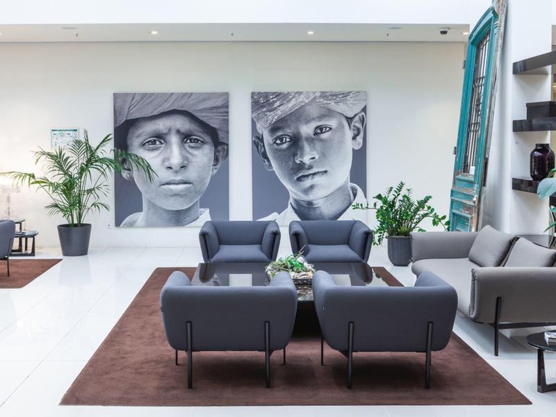 Interior moderno de lobby de hotel con sillones grises, alfombra marrón y grandes retratos en blanco y negro.