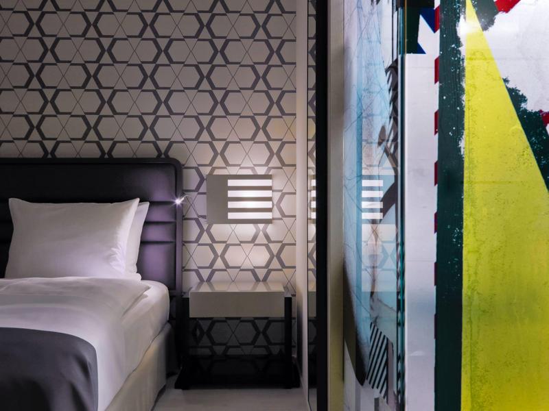 Habitación de hotel moderna con cama individual cómoda, mesita de noche y decoración artística en la pared.