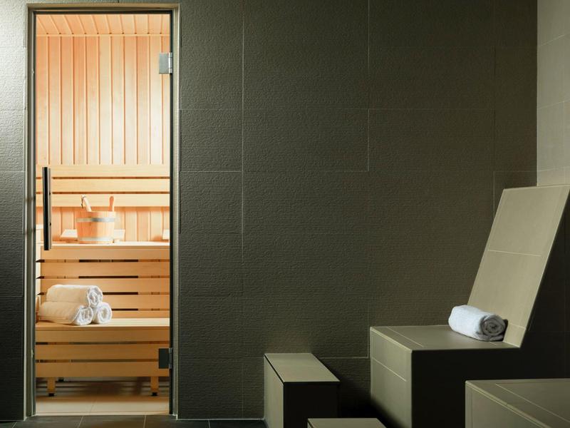 Sala de sauna moderna con banco de madera y tumbona, ambos con toallas dobladas.