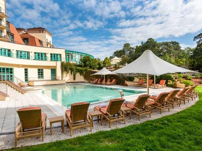 Une piscine d'hôtel avec des chaises longues et des parasols à côté d'un bâtiment à plusieurs étages et d'une pelouse verte.