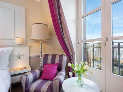 Poltrona accogliente con cuscino accanto alla finestra e tavolino rotondo bianco con fiori nella camera d'hotel.