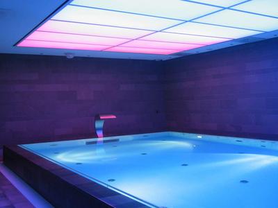 Vasca idromassaggio interna moderna con acqua blu e illuminazione d'ambiente sul soffitto.