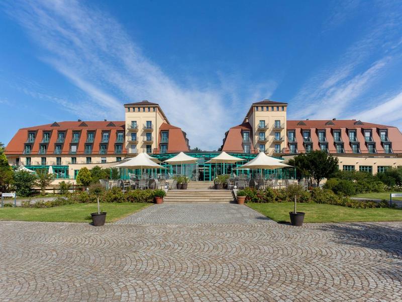 Grande edificio dell'hotel con tetti rossi e terrazza soleggiata sotto un cielo blu.