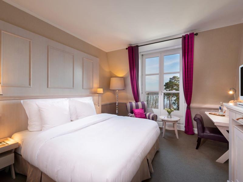 Camera d'albergo accogliente con letto grande, sedia, scrivania e finestra con tende viola.