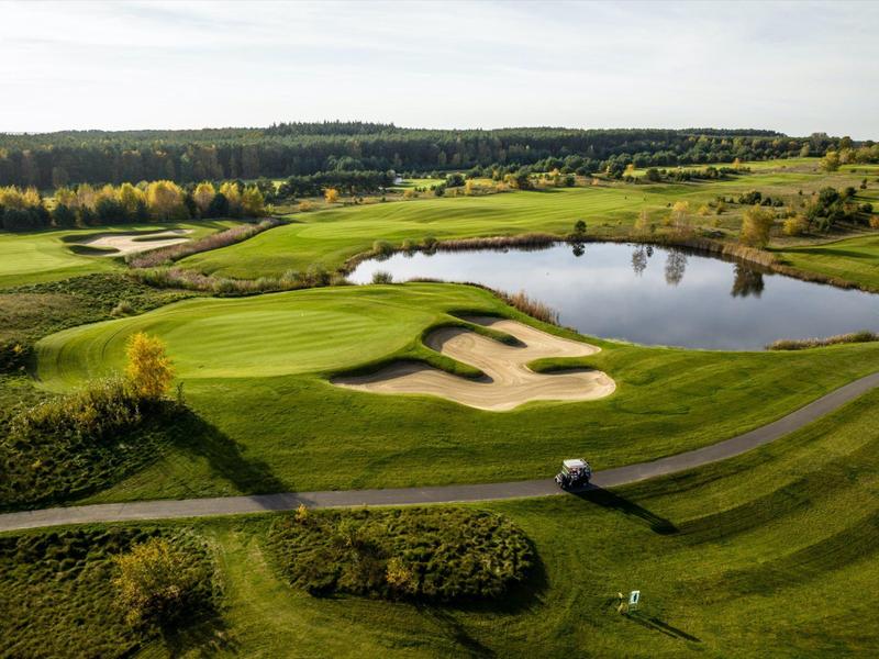 Ampio campo da golf con green curati, bunker di sabbia e un grande ostacolo d'acqua sotto un cielo nuvoloso.