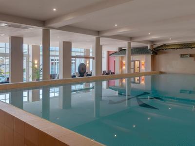 Indoor hotel swimming pool with large windows and a spa-like atmosphere.