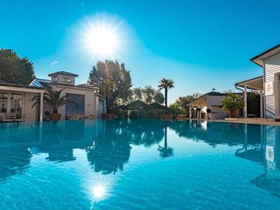 Large hotel pool under sunny sky with palm trees and buildings in the background.