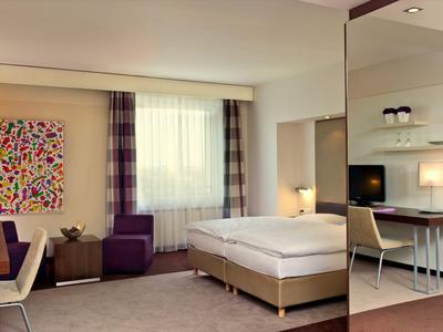 Modernes Hotelzimmer mit Doppelbett, Sitzbereich, Schreibtisch und dekorativem Bild an der Wand.