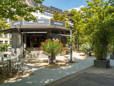 Un espace café extérieur avec des arbres et des plantes dans un environnement urbain ensoleillé.