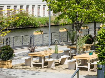 Espace extérieur d'un hôtel avec tables en bois, bancs et plantes vertes au bord d'une rivière.