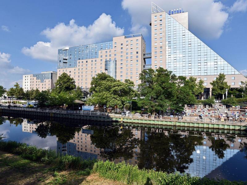 Bâtiment d'hôtel moderne au bord de la rivière avec surface d'eau réfléchissante et rives verdoyantes.