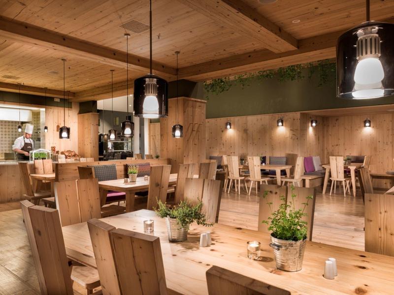 Espace restaurant d'hôtel confortable avec mobilier en bois, lampes suspendues et plantes sur les tables.