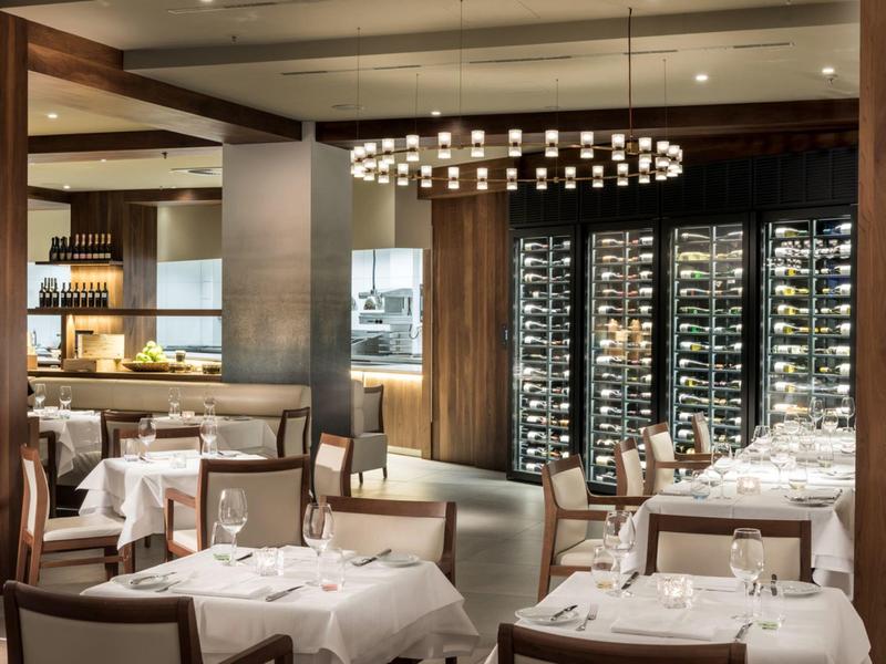 Restaurant élégant avec nappes blanches, accents en bois et un lustre moderne.