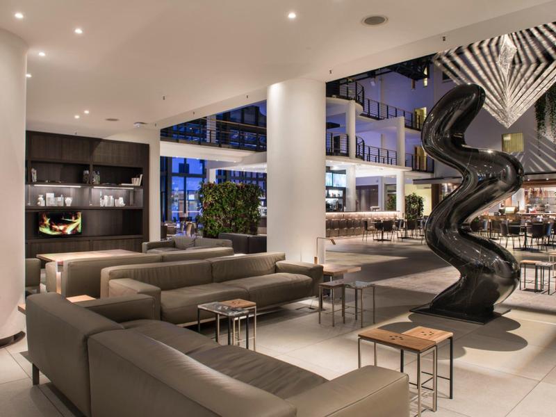 Hall d'hôtel moderne avec canapés, sculpture et grandes fenêtres.