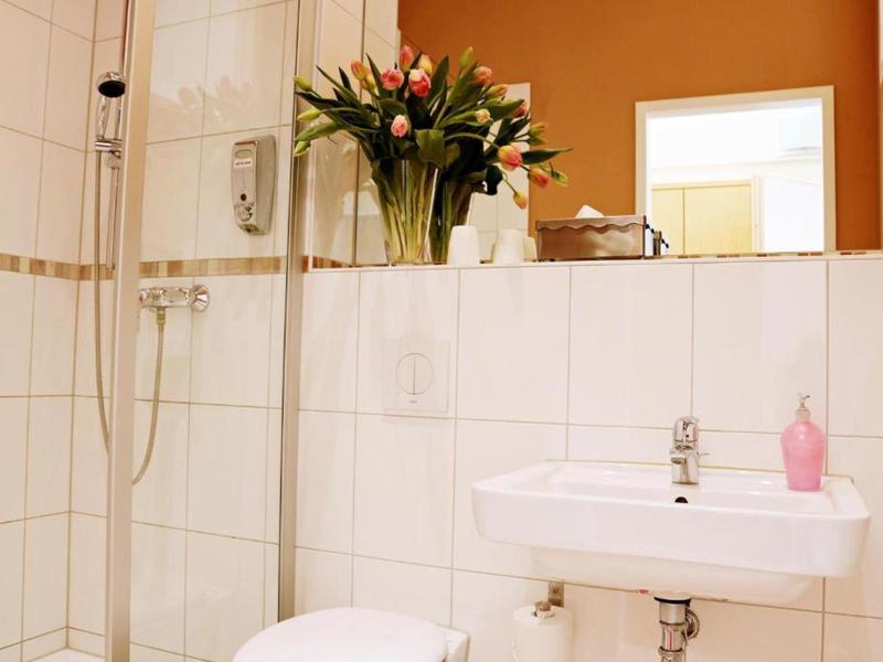 Helles Badezimmer mit weiß gekachelten Wänden, kleinem Waschbecken und Blumen auf der Ablage.