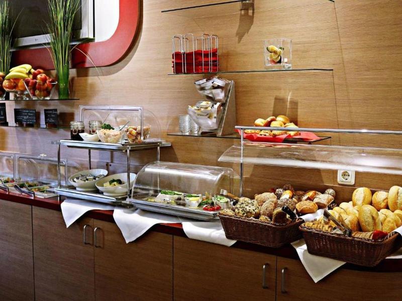 Buffet mit verschiedenen Brötchen, Gebäck, Obst, Aufschnitt und Gläsern auf Holztheke.