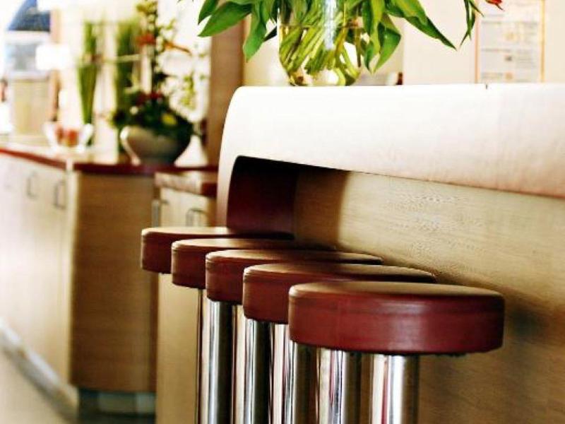 Vier rote Barhocker mit Metallbeinen stehen an einem Holzthekenrand, darüber ein Blumenstrauß.