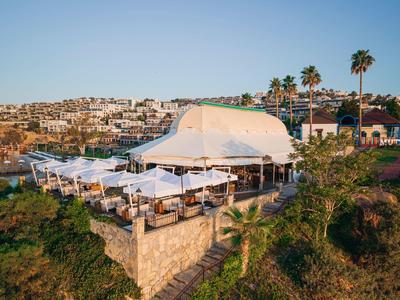 Openluchtrestaurant met witte parasols op een klif met uitzicht op stad en zee.