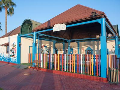 Kleurrijk gebouw met roodbruine dak en meerkleurige omheining onder blauwe lucht met palmbomen