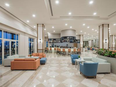 Moderne hotellobby met zitgedeeltes, bar en grote ramen bij schemering.