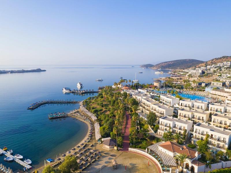 Luchtfoto van een kustresort met zwembad, strand en rustig blauw zeezicht.