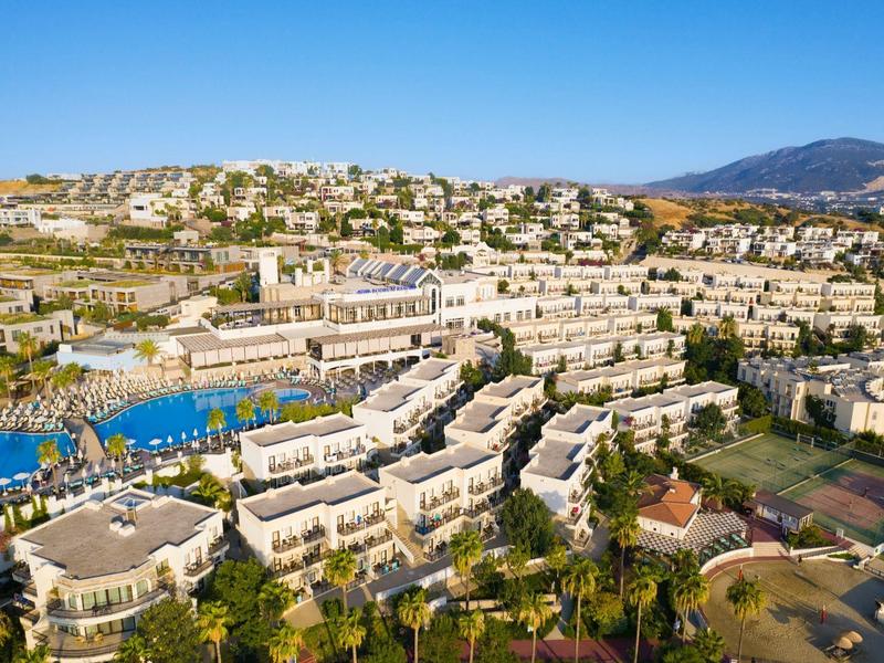 Uitgestrekt hotelcomplex op de heuvel met zwembaden en palmbomen onder een blauwe lucht