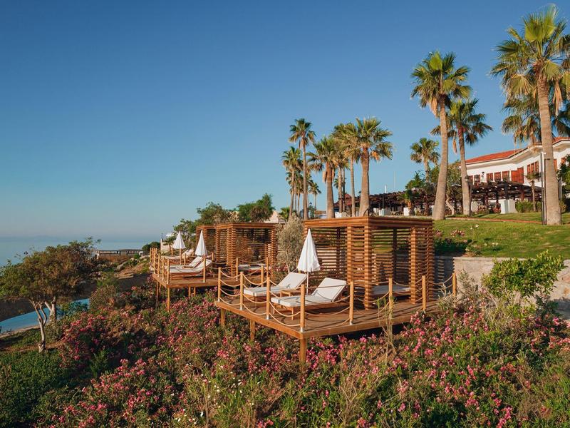 Strandligbedden op houten platformen met witte parasols en palmbomen bij een resort.