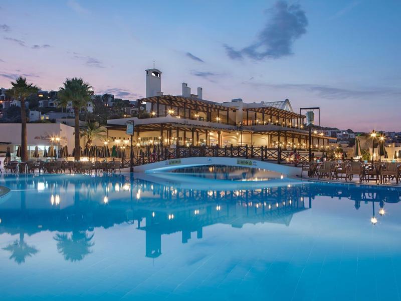 Avondzicht op een modern hotel met verlicht zwembad en brug.