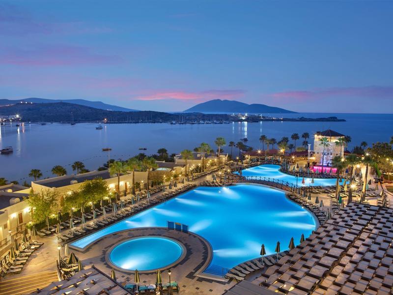 Luxe hotelzwembad met ronde en gebogen vormen aan de kust bij schemering.