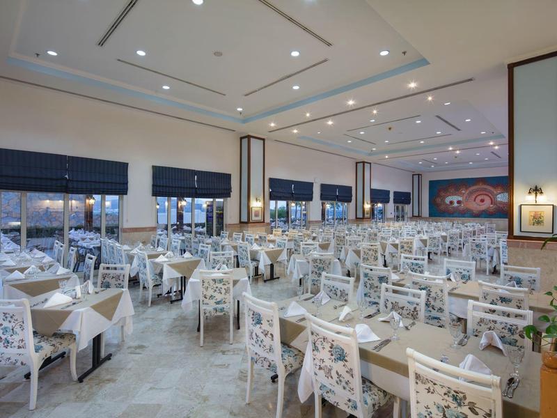 Grote elegante eetzaal met veel tafels en witte stoelen, moderne verlichting.