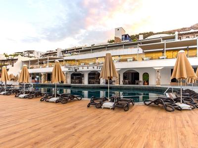 Beach loungers and closed umbrellas on a wooden deck overlooking a hotel building