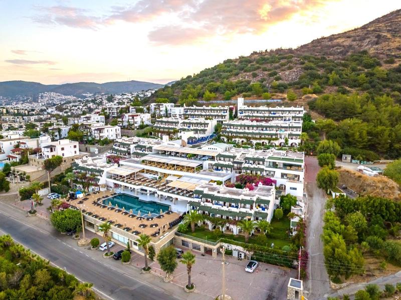 Large hillside hotel with pool, surrounded by trees and city views.