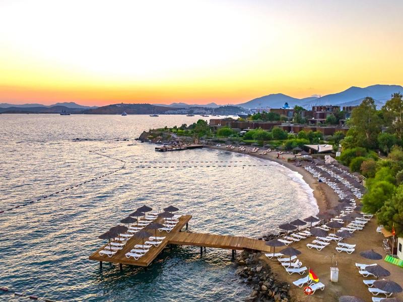 Sunset at a beach with lounge chairs, dock, and calm sea near a hotel.