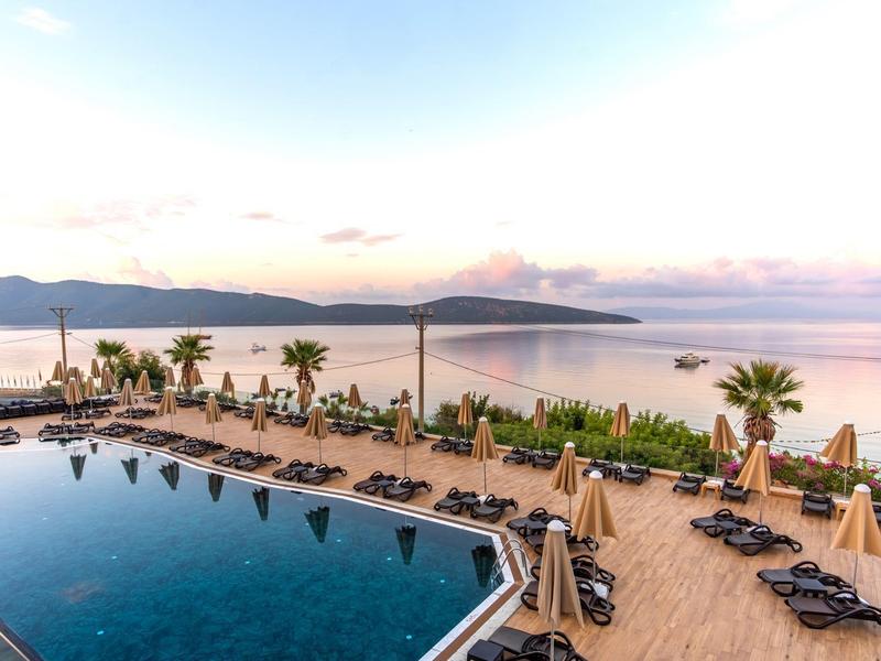 Hotel pool with lounge chairs and umbrellas overlooking the sea at sunset.