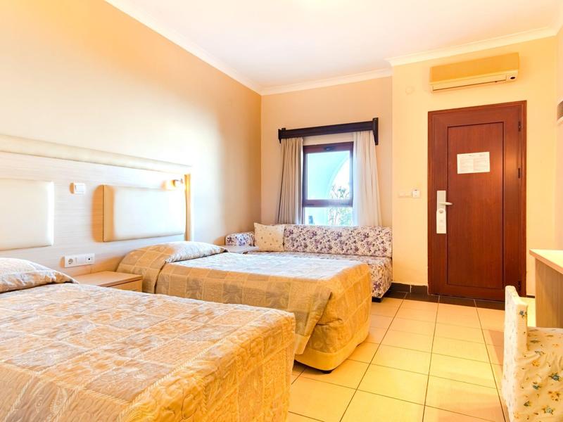 Bright hotel room with two single beds, tiled floor, and air conditioning above the door.