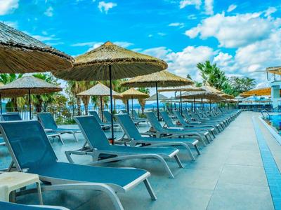 Rangée de chaises longues vertes et parasols en paille au bord de la piscine sous un ciel bleu.