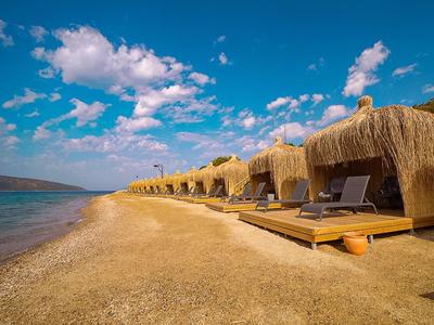 Leerer Sandstrand mit Liegen unter Strohdächern und blauem Himmel mit Wolken.