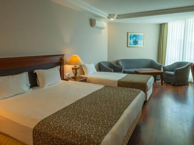 Chambre d'hôtel avec deux lits, canapé, fauteuils, sol en bois et lampe sur table de chevet.